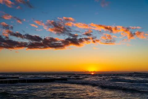 Orange clouds sunset sky above waves Baltic sea. Magic hour. Stock Photos