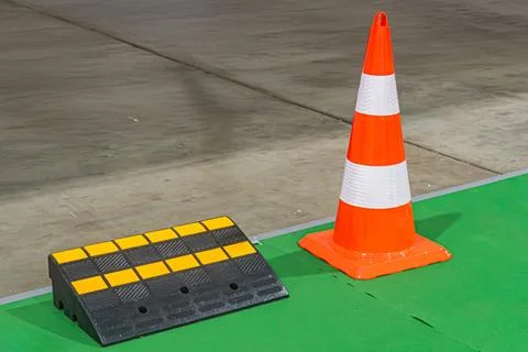An orange cone on a black platform against a green and yellow striped floor,  Stock Photos