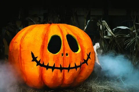 Orange creepy scary pumpkin on stack of hay or straw and smoke floating aro.. 스톡 사진