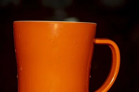 Orange cup featuring wet surface droplets for kitchen beverage use. Stock Photos