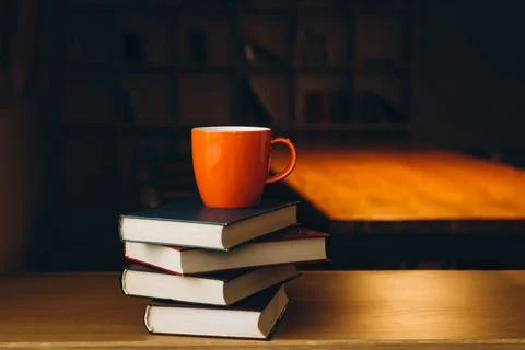 An orange cup on a stack of books on a dark library background. Stock Photos