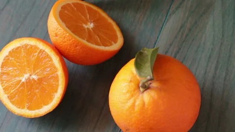 Orange cut in half and other oranges on ultramarine colored wooden background Stock Footage 152223909