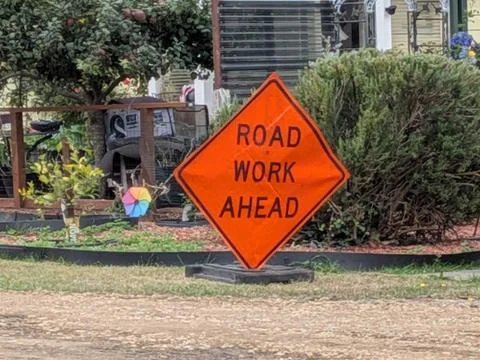 Orange diamond “Road Work Ahead” sign standing near a decorated front yard Stock Photos