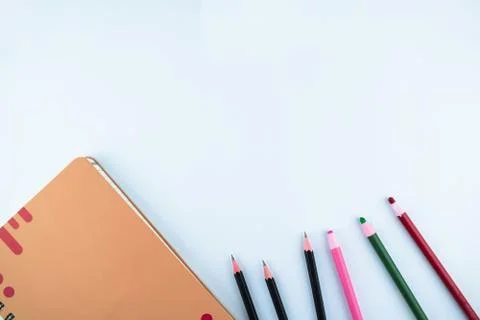 An orange diary along side some black pencils and different colored crayons o Foto stock