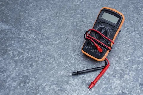 Orange digital multimeter with red test probe leads on textured gray metal ba Stock Photos