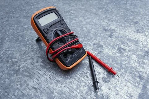 Orange digital multimeter with red test probe leads on textured gray metal .. Stock Photos