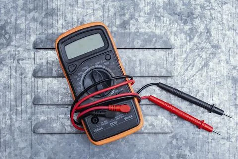Orange digital multimeter with red test probe leads on textured gray metal .. Stock Photos