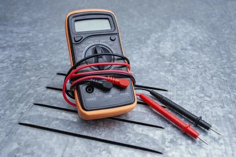 Orange digital multimeter with red test probe leads on textured gray metal ba Stock Photos