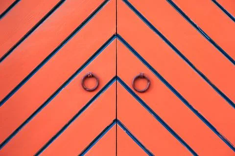 Orange double door and ring knockers. Diagonal black and blue stripes in Stock Photos