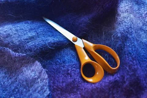 Orange dressmaking scissors lying on soft blue mohair wool fabric Stock Photos