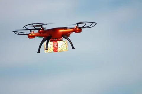 Orange drone with gift box on the cloudy sky background Stock Photos
