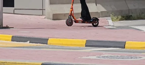 Orange e-scooter rides on a paved path with a yellow and black curb Video stock 311892103
