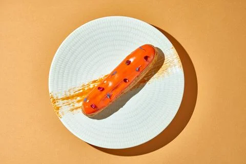 Orange eclair in a plate on an orange background Stock Photos