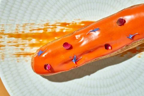 Orange eclair in a plate on an orange background Stock Photos