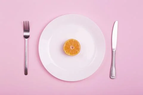 Orange on an empty white plate on a pink background. Food minimal creative ar Stock Photos