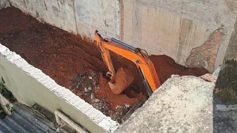 Orange excavator digging deep soil foundation in urban construction video Video stock 339374455