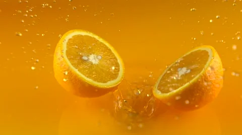 Orange falls on orange juice surface and splits into halves. Slow motion video Stock Footage 61137589