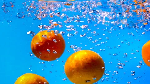 The orange falls into the water on the blue background. Slow motion. 库存影片 145350184