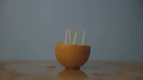 Orange With Five Candles In It Being Lit, Then Spun and Blown Out Stock Footage 136992514