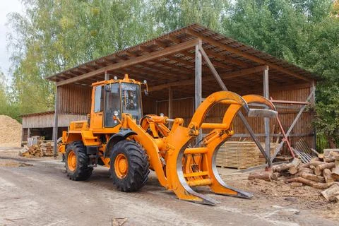 Orange forestry loader with a claw attachment parked at a sawmill near a wood Stock Photos
