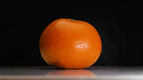 Orange fruit on white surface is spinning in dark scene Stock Footage 262261565