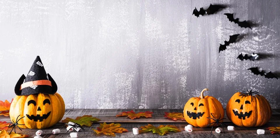 Orange ghost pumpkins with witch hat on gray wooden board background with bat Foto stock