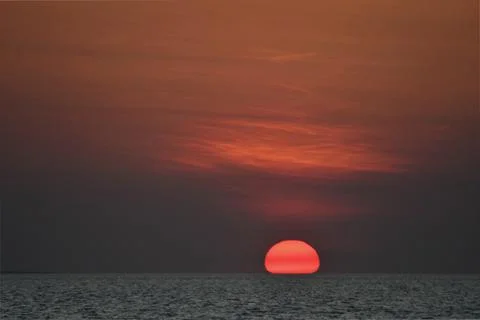The orange globe of the setting sun over the sea. Stock Photos