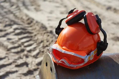 Orange hard hat with attached ear muffs and protective goggles resting on a.. Stock Photos