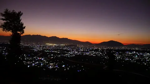 Orange horizon of sunset sky with night city lights and mountains Stock Footage 248140336