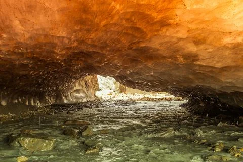 Orange ice cave carved into the Vallelunga glacier crossed by a stream Stock Photos