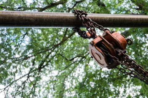Orange industrial hook chains attached to a pulley and green tree background Stock Photos