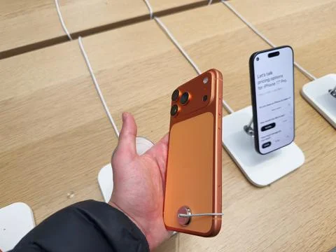 Orange iPhone 17 Pro held in hand at retail display with another phone on s.. Stock Photos