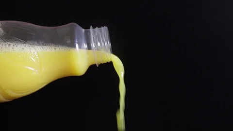 Orange juice flowing from a plastic bottle on a black background. Stock Footage 101669872