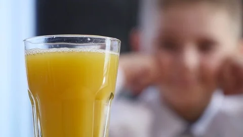 Orange juice pouring into glass. little boy background. selective focus Stock Footage