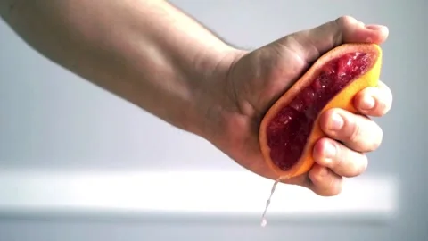 Orange juice splashes from half of fruit in hand, close up of squeezing orange Видео 336588948