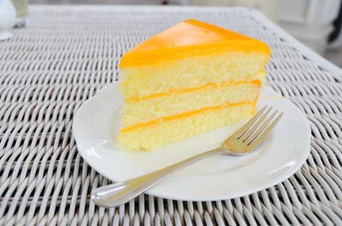 Orange layer cake on white plate put on rattan table. Stock Photos
