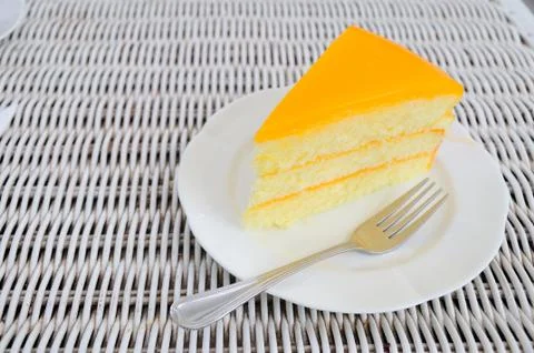 Orange layer cake on white plate put on rattan table. Stock Photos