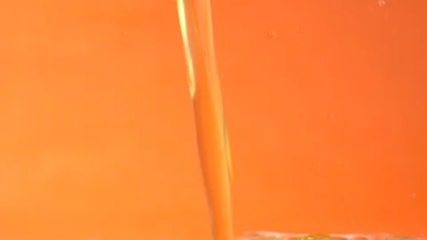 Orange Lemonade pouring down into clear glass standing on yellow background in Stock-Footage 123368829