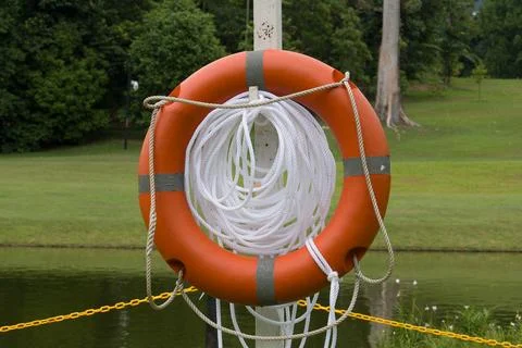 Orange life ring hangs on pole beside water Stock Photos