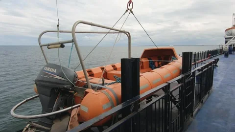 Orange lifeboat secured on a ferry deck over calm waters, ready for emergency Stock Footage 289926476