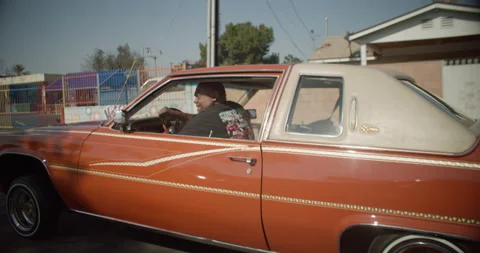 Orange Lowrider Car Bouncing Its Hydraulics Driving Down The Street In Stock Footage 155263066