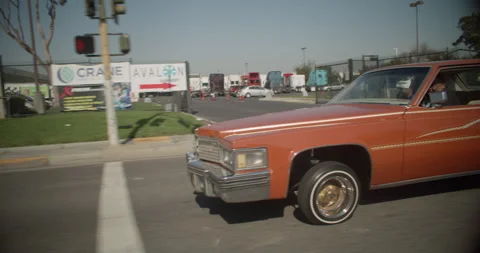 Orange Lowrider Car Bouncing Its Hydraulics Driving Down The Street In Stock Footage 155263167