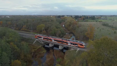 Orange modern electric train rides in nature over the river on the bridge. Vídeo Stock 100101398