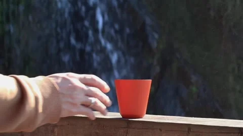 Orange mug against the background of a waterfall, a man's hand takes a mug Stock Footage 290165372