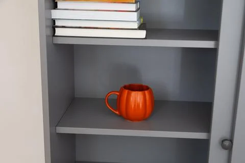 Orange mug on gray bookshelf under stack of books. Color accent, creativity,  Stock Photos