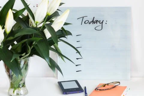 Orange notebook, glassses, blue e-book with PLANS FOR TODAY desk and a bouque Stock Photos