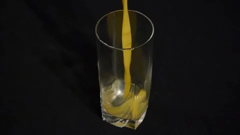 Orange or pineapple juice being poured in a tall glass on a black background 스톡 동영상 106204992