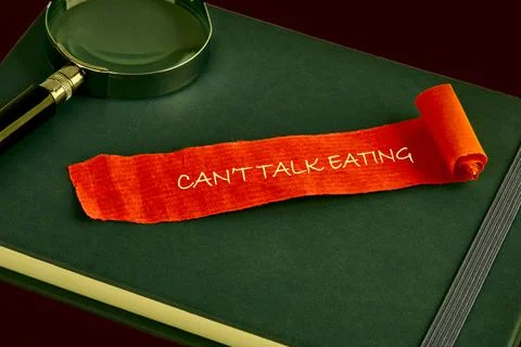 An orange paper scroll with the phrase Cant Talk Eating rests on top of a dark 库存照片