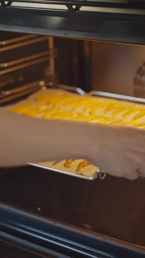 Orange peel strips dry on parchment paper as person slides baking tray into oven Stock Footage 340522010