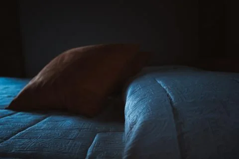 Orange pillow on a bed with low blue soft light Stock Photos
